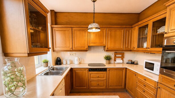 A kitchen with wooden cabinets, a stainless steel sink, a microwave, and a hanging light fixture.