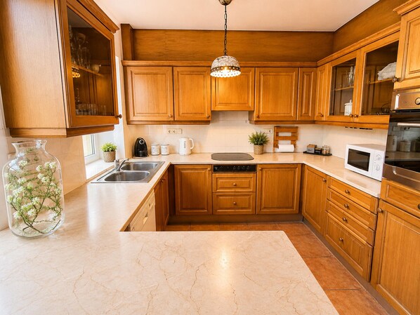 Una cocina con armarios de madera, un lavamanos de acero inoxidable, un microondas y una lámpara colgante.
