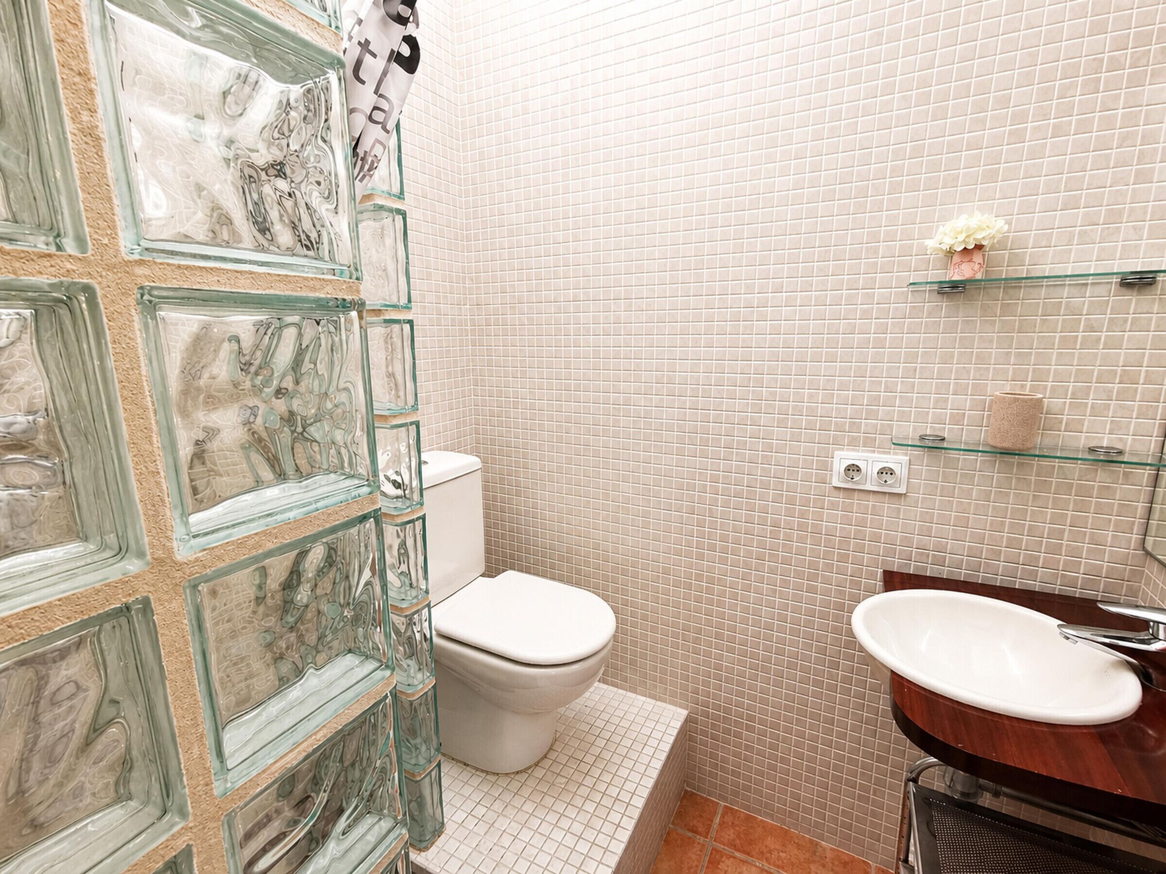 Un baño con cabina de ducha de vidrio, inodoro, lavamanos y pared con azulejos.