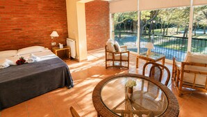 A hotel room with a bed, a small table, a chair, and a balcony with a view of a pool and trees.
