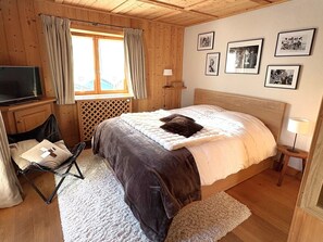 Una habitación acogedora con cama, televisión, ventana con cortinas e imágenes enmarcadas en la pared.