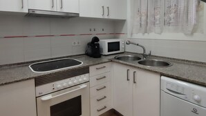 A compact kitchen with white cabinets, a built-in oven, a microwave, a coffee maker, and a dishwasher. - Cozy Apartment with Terrace Near Beach and Shops in Costa Brava (Platja d'Aro)