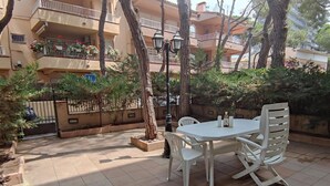 An outdoor patio with a white table and chairs, surrounded by trees and a tiled floor. - Cozy Apartment with Terrace Near Beach and Shops in Costa Brava (Platja d'Aro)