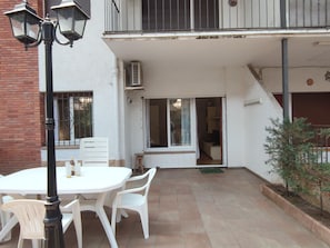 An outdoor patio with a white table and chairs, a black lamp post, and a small plant.