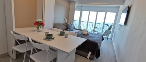 A modern hotel room with a dining area, a bed with a view, and a balcony.
