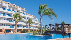 Un hôtel à plusieurs étages, doté d’une piscine et bordé de palmiers.