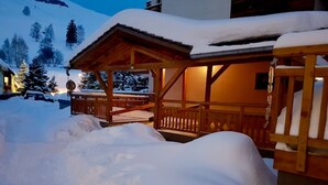 Eine Holzchalet mit überdachter Veranda und einer mit Schnee bedeckten Terrasse.