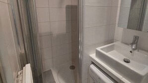 Ein Badezimmer mit Duschkabine aus Glas, einem weißen Waschbecken und einem Spiegel darüber.