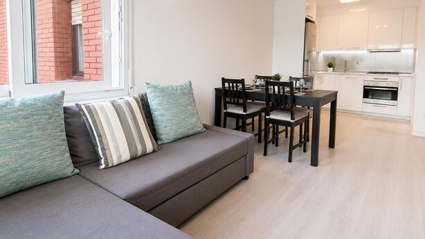 Um apartamento moderno com um sofá cinzento, mesa de jantar e cozinha branca.