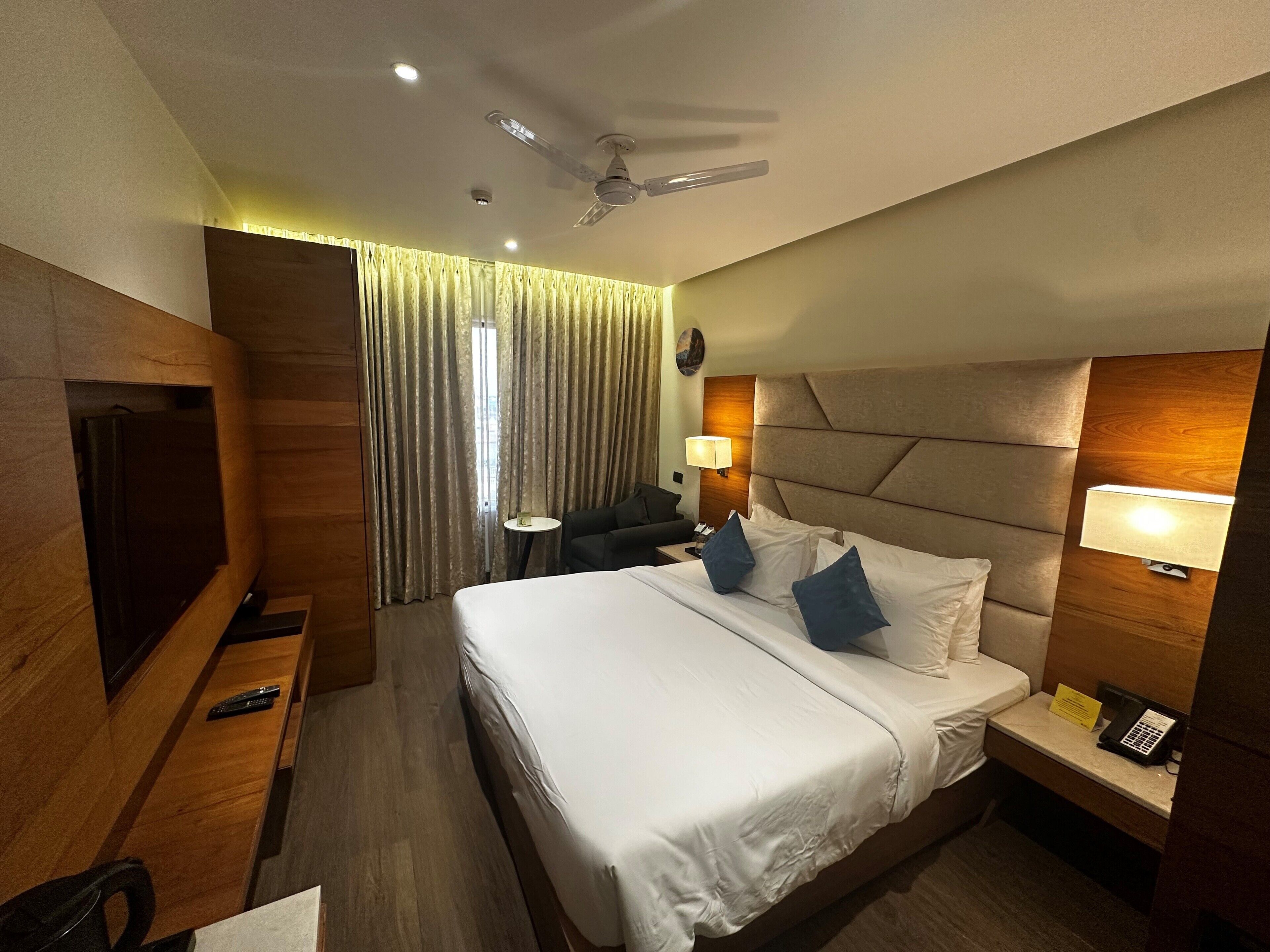 A hotel room with a bed, bedside table, lamp, and a TV on a wooden cabinet.