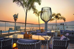 A rooftop terrace with outdoor seating, a decorative metal sculpture, and a view of the sunset over a body of water. - The Fern Residency Ajmer  (Ajmer)