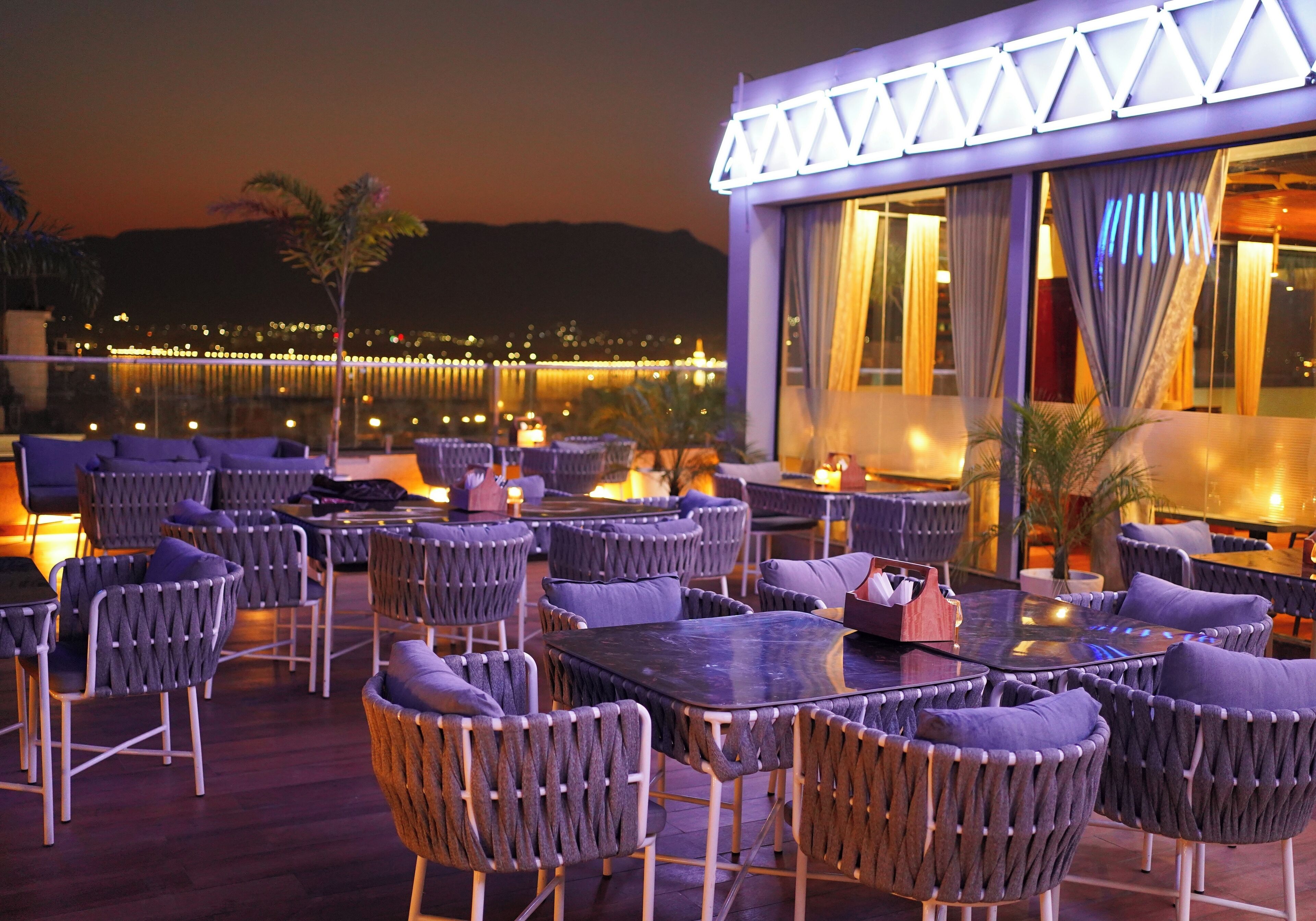 An outdoor seating area with tables and chairs, a pool, and a building with illuminated windows.