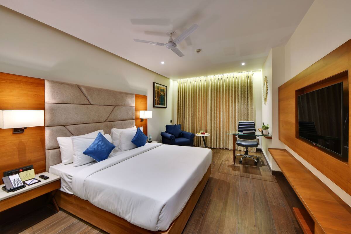 A hotel room with a large bed, a desk with a telephone and notepad, a chair, a TV, and a ceiling fan.