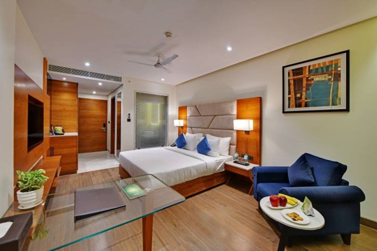 A hotel room with a bed, a desk, a chair, a TV, and a painting on the wall.