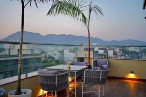 Una terrazza sul tetto con un tavolo e sedie, una pianta in vaso e vista sulla città e sulle montagne sullo sfondo.