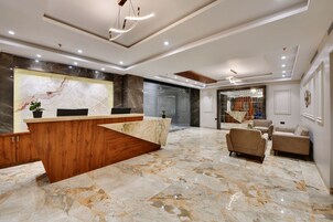 A modern lobby with a marble reception desk, sofas, and a staircase leading to upper floors.