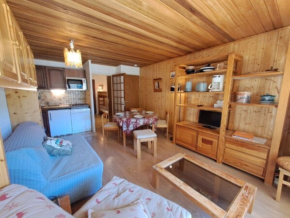 Un espacio habitable compacto con kitchenette, comedor y televisor.