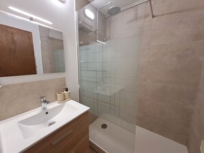Ein modernes Badezimmer mit einer gläsernen Duschkabine, einem weißen Waschbecken und einem Spiegel darüber.