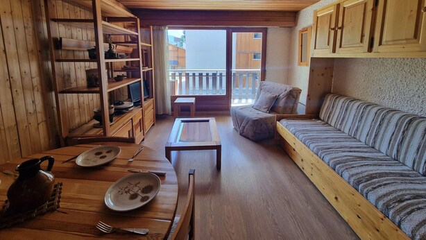 Ein gemütliches Zimmer mit Holzböden, einem Sofa, einem Sessel, einem Esstisch und einem Bücherregal.