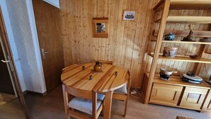 Ein Essbereich mit Holzboden, ausgestattet mit einem runden Tisch und Stühlen, einem Holzkabinett mit Regalen und einem kleinen gerahmten Bild an der Wand.