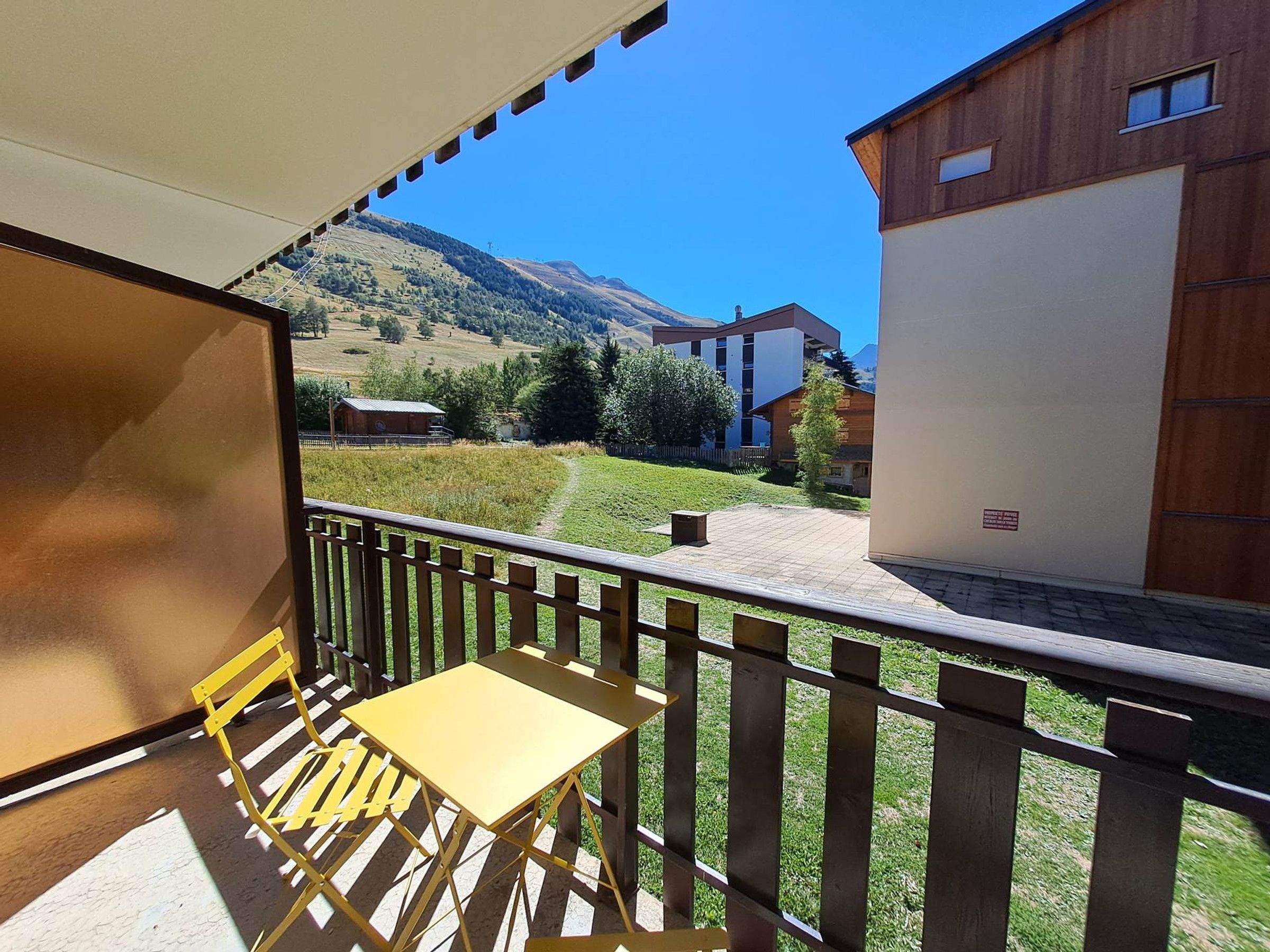 A balcony with a wooden railing, a yellow table, and a view of a mountain and buildings.