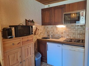 Una cocina compacta con armarios de madera, un microondas, una estufa y un lavavajillas.