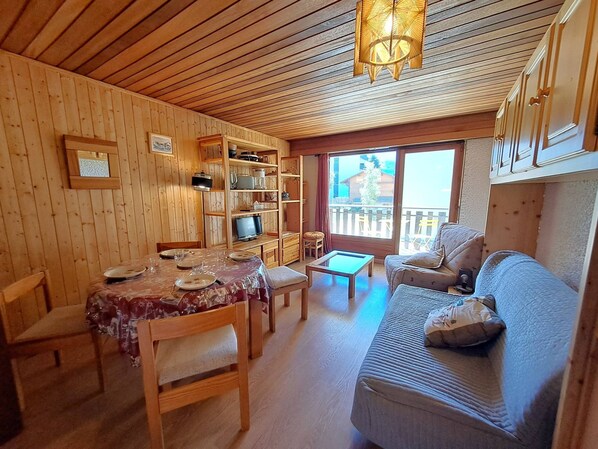 A wooden interior with a dining table, chairs, a sofa, and a television.