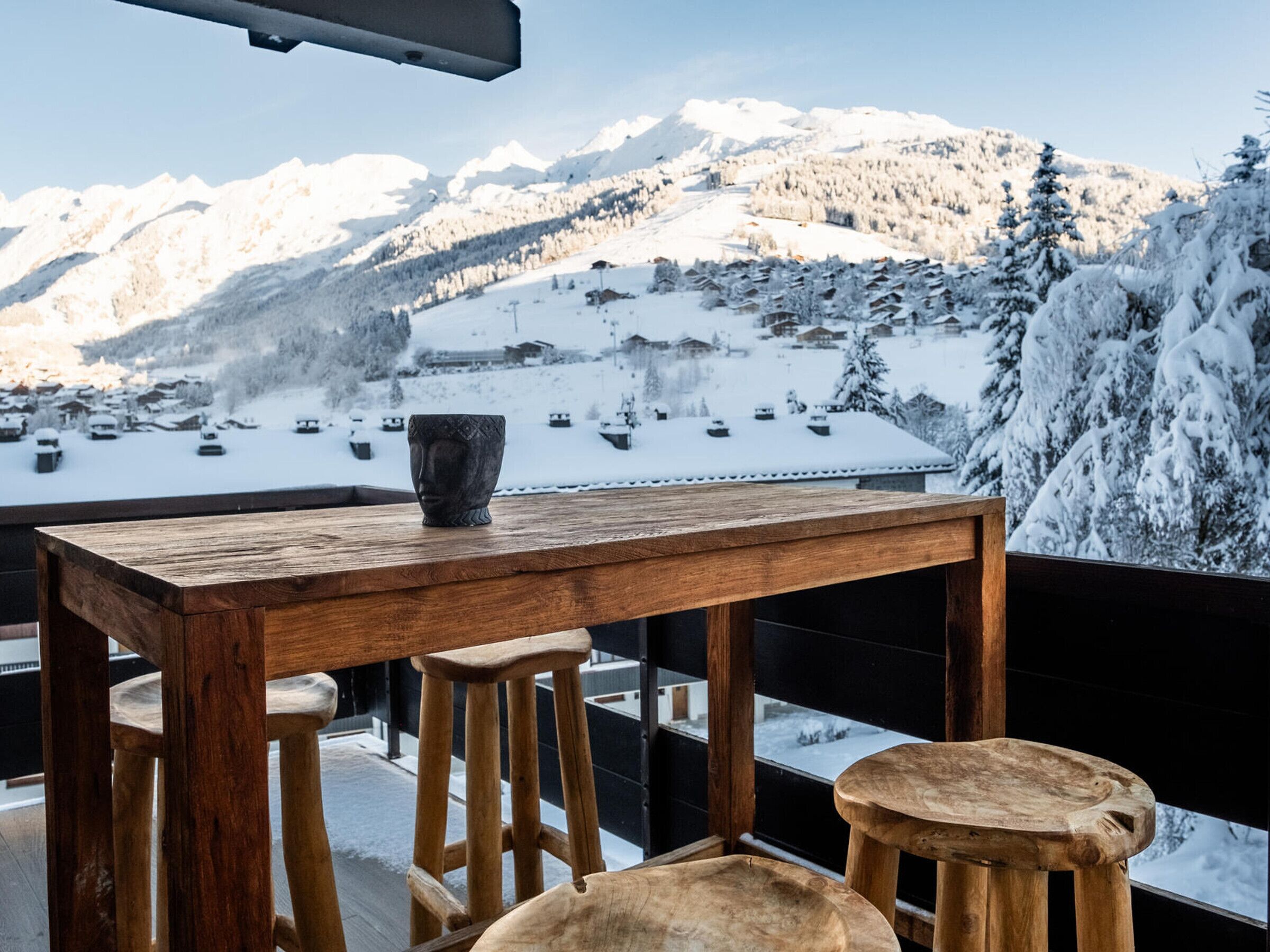 A wooden table with a vase, two stools, and a view of snow-covered mountains.