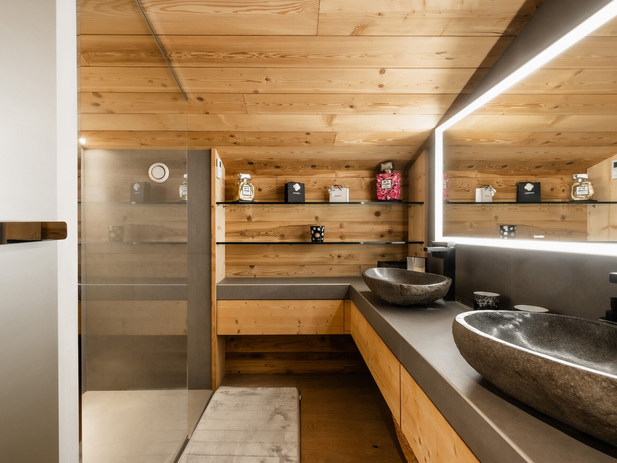 A modern bathroom with wooden paneling, a large mirror, and a stone sink.
