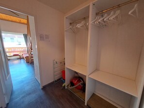 Ein begehbarer Kleiderschrank mit offenen Regalen, ein Staubsauger und eine Bank mit rotem Kissen.