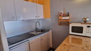 Una cocina compacta con armarios blancos, encimera negra, pileta, lavavajillas y microondas.