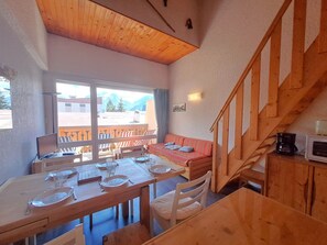 Een eethoek met een houten tafel voor twee personen, een rode bank en een trap met houten leuningen.
