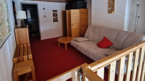Una sala de estar acogedora con techo de madera, un sofá, una mesita, una silla de madera y un armario.