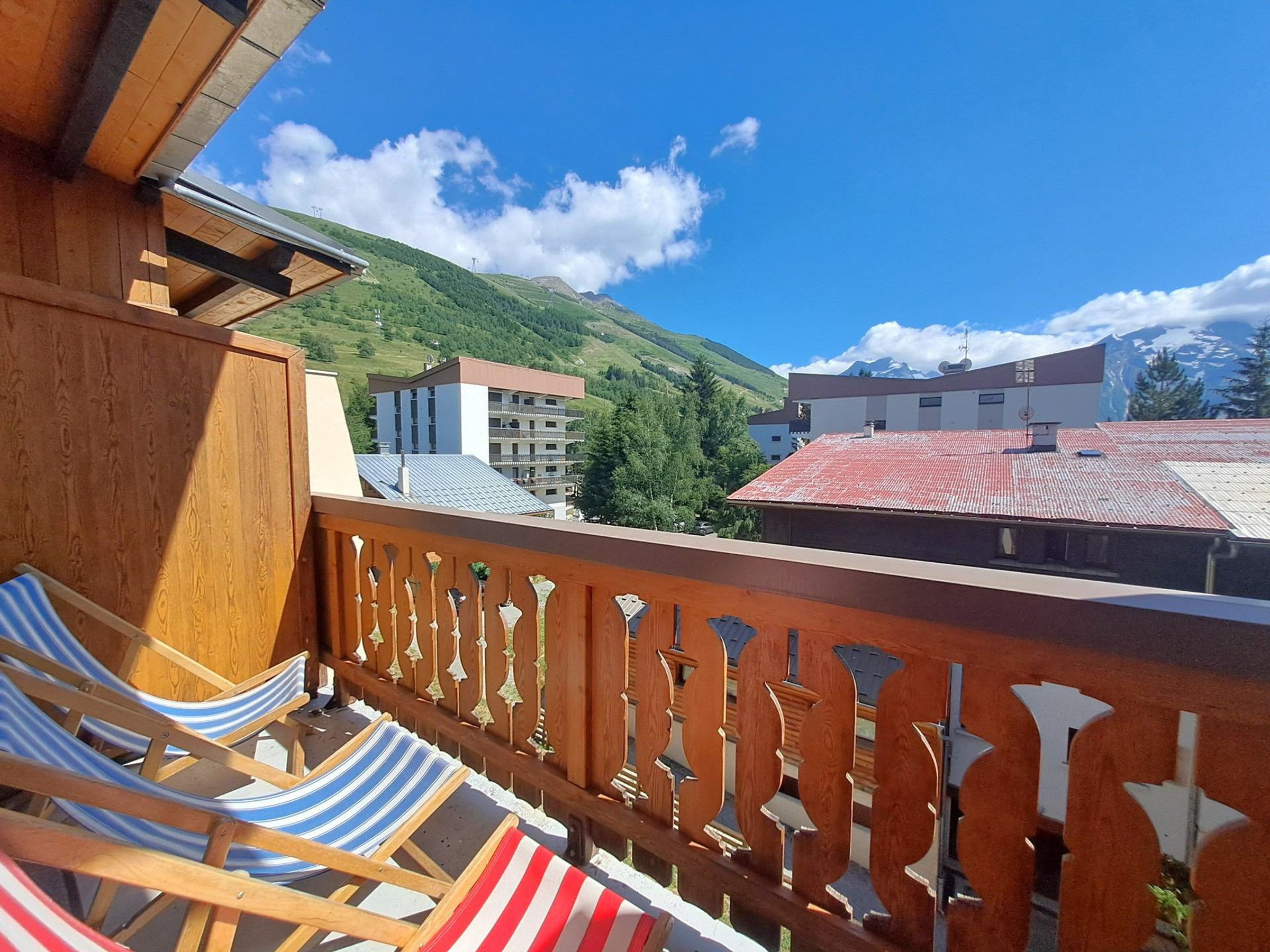 Un balcon avec des fauteuils de jardin à rayures, une balustrade en bois et une vue sur les bâtiments et les montagnes.