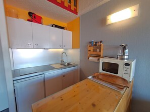Een kleine keuken met witte kasten, een roestvrijstalen spoelbak, een magnetron en een houten aanrecht.