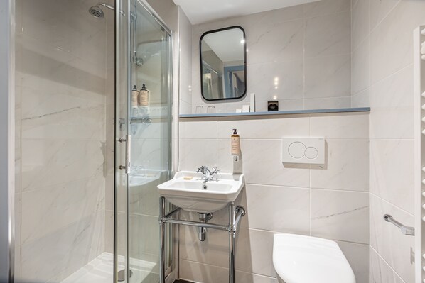 Un baño moderno con cabina de ducha de vidrio, un lavamanos blanco con grifería cromada y un inodoro.