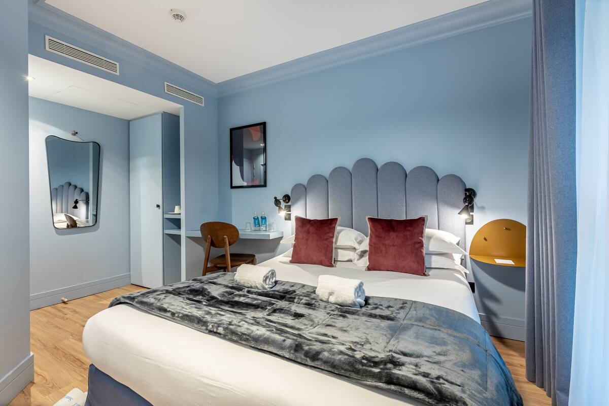 A modern bedroom with a large bed, a bedside table, a chair, a mirror, and a small desk with a chair.