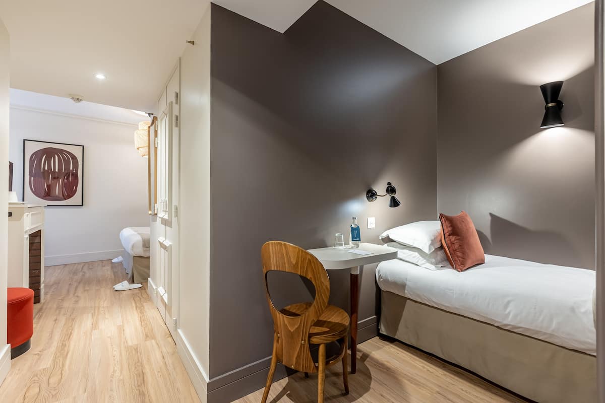 A modern bedroom with a bed, a desk, and a chair. There is a wall-mounted lamp and a painting on the wall.