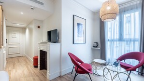 A modern hotel room with a fireplace, red chairs, a television, and a large window with curtains. - Le Nest by Sweett (Paris)