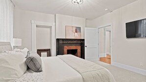 Ein Schlafzimmer mit einem großen Bett, einem Kamin, einem an der Wand befestigten Fernseher und einer Tür zu einem anderen Raum.