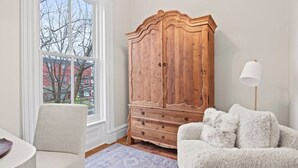 Une pièce comprenant une grande armoire en bois, un fauteuil blanc, un canapé moelleux et un lampadaire.