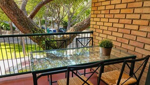 Une terrasse extérieure avec une table et des chaises en verre, un mur en briques et un arbre.