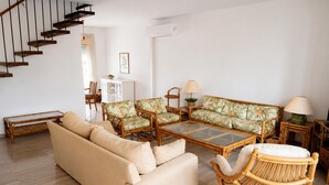 Un salon comprenant un canapé, des fauteuils, une table basse, un fauteuil en osier et un escalier.