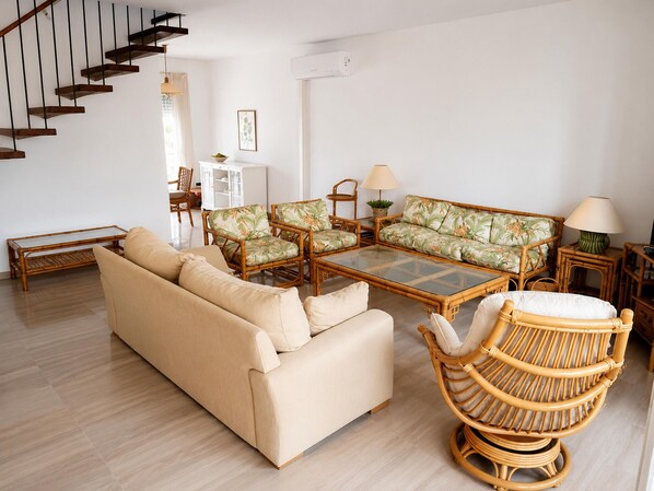 A living room with a sofa, chairs, a coffee table, a wicker chair, and a staircase.