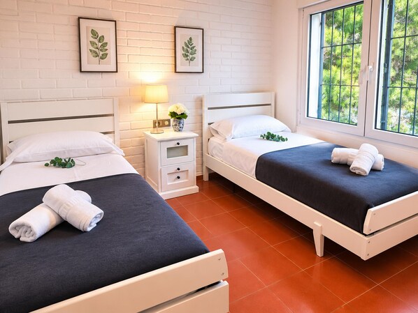 A hotel room with two beds, a nightstand with a lamp, and a window with a view of trees.