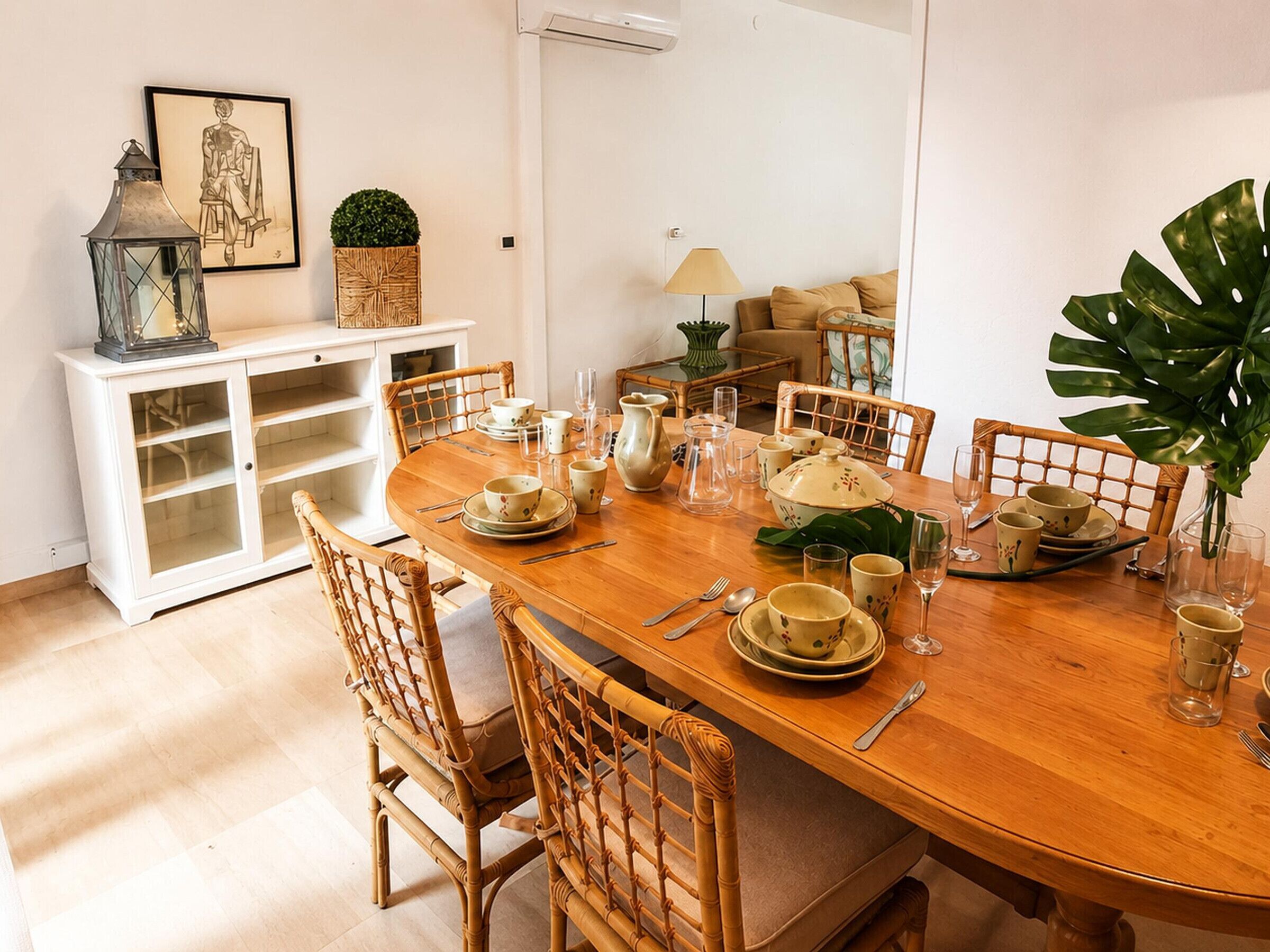 A dining area with a wooden table set for four, surrounded by wicker chairs.
