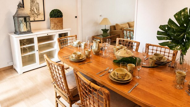 Un coin repas avec une table en bois dressée pour quatre personnes, entourée de chaises en osier.