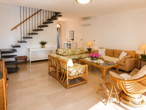 A living room with a staircase, a sofa, a coffee table, and wicker furniture. - Stunning 6-Bedroom Villa in Platja d’Aro, Steps from Beach with Terrace (Platja d'Aro)