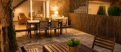 An outdoor patio with a dining table and chairs, a potted plant, and a staircase leading to an upper level.