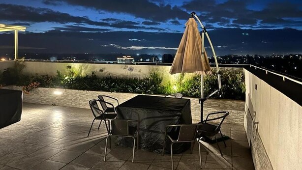 An outdoor patio with a table and chairs, a covered umbrella, and a view of the city skyline at night. - Lux Suites Perry West Luxurios Apartment (Nairobi)